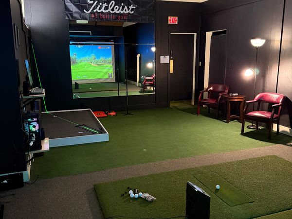 Indoor golf simulator setup with seating area and equipment.