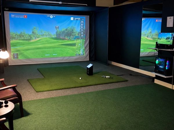 Indoor golf simulator setup with artificial turf and a large screen.