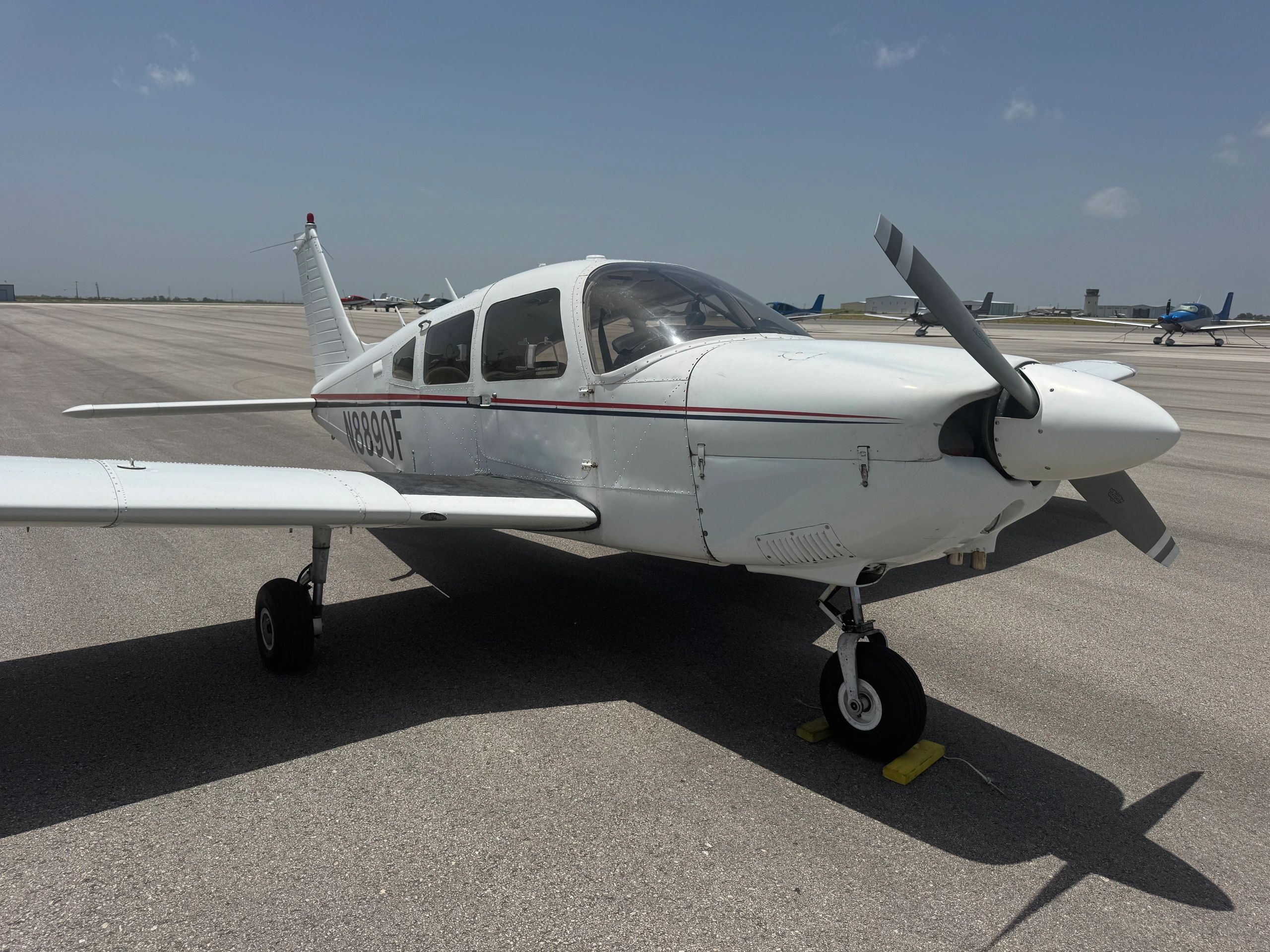 Small white airplane on tarmac under clear sky.