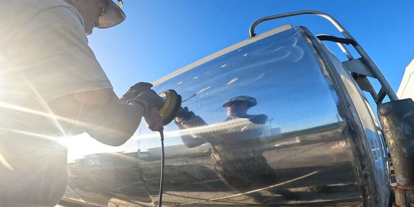 Worker polishing a large metal surface outdoors.
