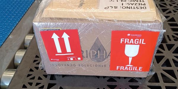 A fragile package wrapped in plastic with handling labels on a conveyor.