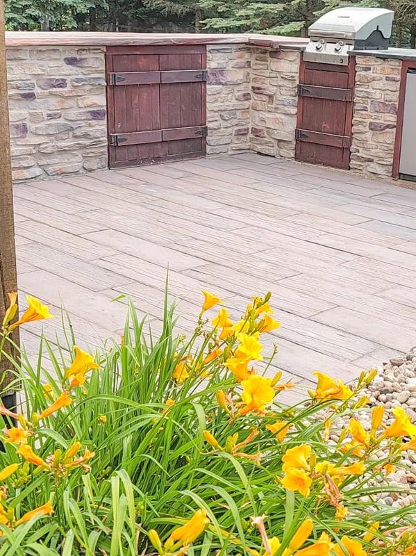 Outdoor patio with yellow flowers and stone wall with wooden doors.