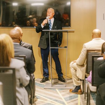 Man in suit speaking at a podium in front of an audience.