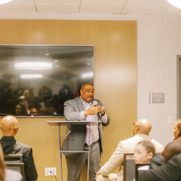 Man speaking at a podium to an audience in a conference room.