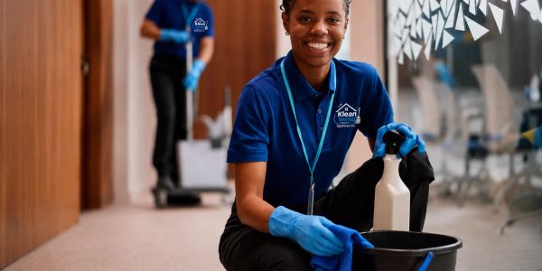 Smiling cleaner kneeling with cleaning supplies in office.