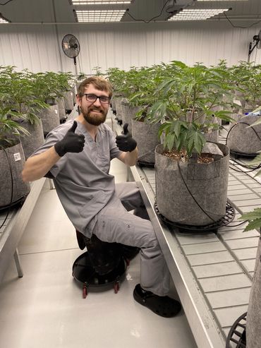 Man in gray scrubs giving thumbs up in an indoor plant nursery.