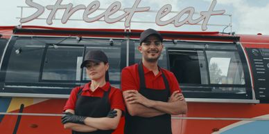 Two food truck workers posing confidently in front of a colorful street food truck.