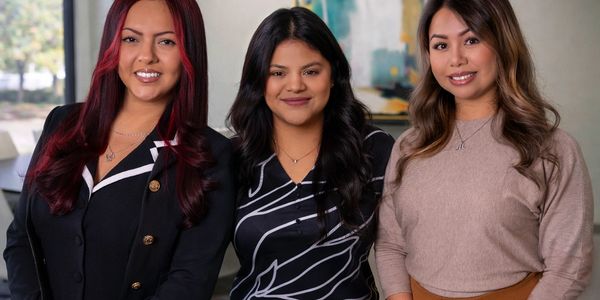 Three women smiling together in a cozy indoor setting.