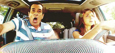 Two people in a car, one shocked and one focused on driving.
