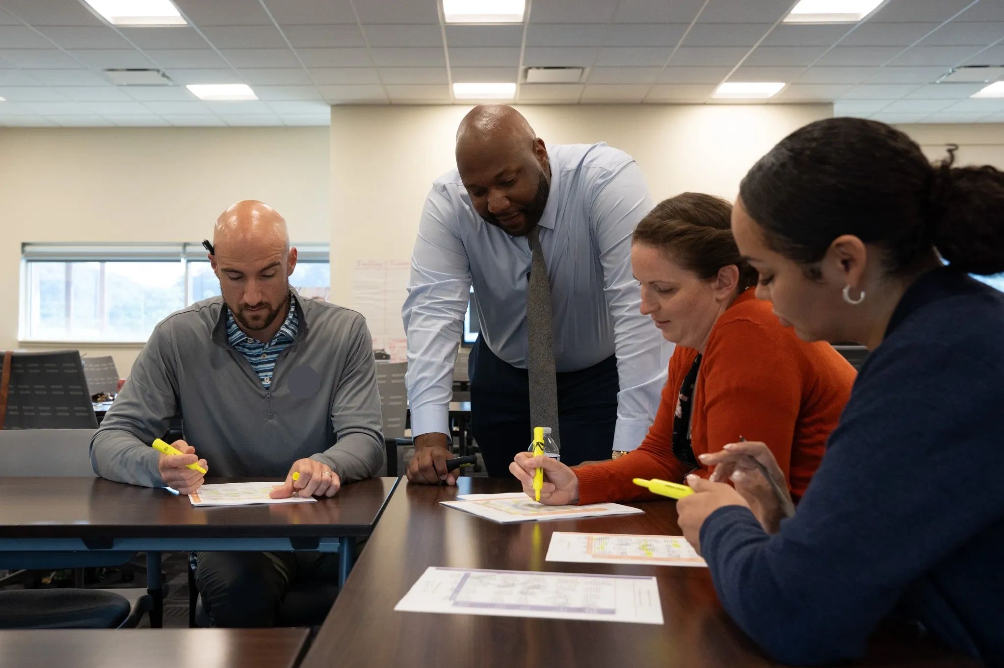 Four adults collaborating over documents with yellow highlighters in a meeting room.