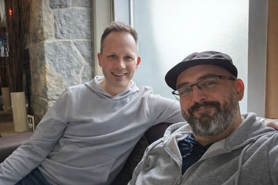 Two men sitting comfortably indoors, smiling at the camera.