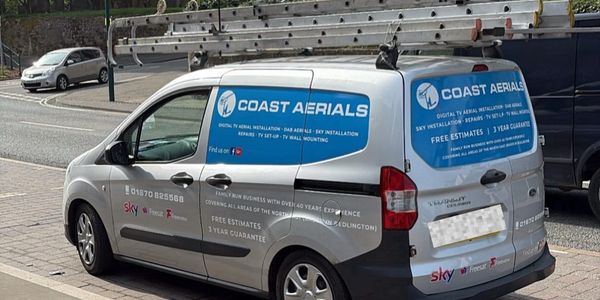 Silver Coast Aerials van with ladders on top parked on street.