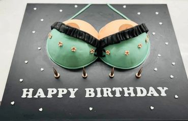 A humorous birthday cake shaped like a woman's chest in a green bra.