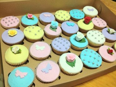 Box of pastel-colored cupcakes decorated with flowers, butterflies, and silver beads.