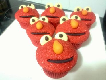 Cupcakes decorated to look like Elmo with red sugar, eyes, orange nose, and black mouth.