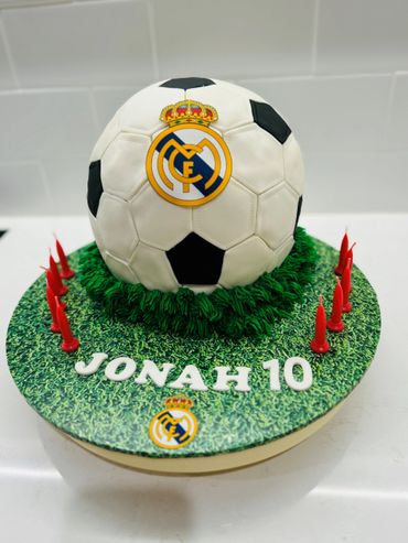 Soccer ball cake with Real Madrid logo and "Jonah 10" on a grass-themed base.