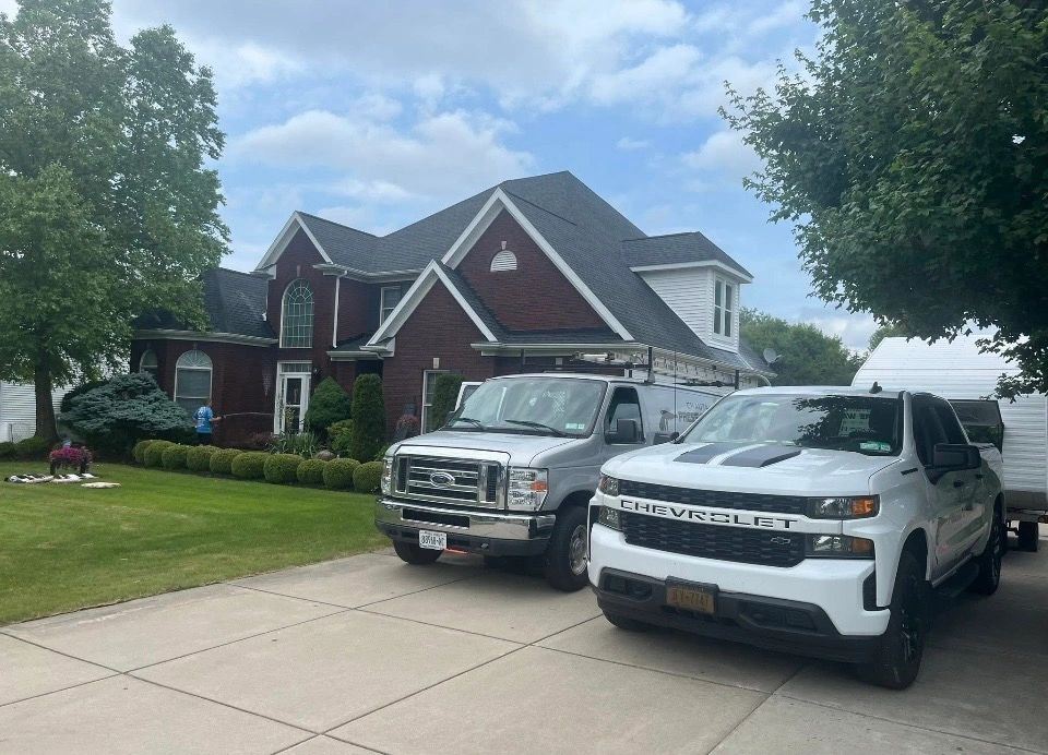 A white Chevrolet truck and a silver van parked in front of a brick house.