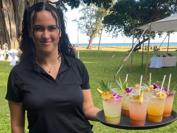 Woman holding tray of colorful cocktails outdoors at event.