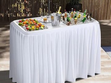 A white draped table with drinks and fruit skewers.