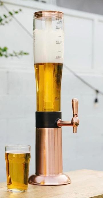 A tall beer dispenser with a glass of beer on a wooden table.