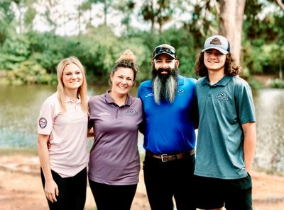Four people in casual company-branded polo shirts pose outdoors by a lake.