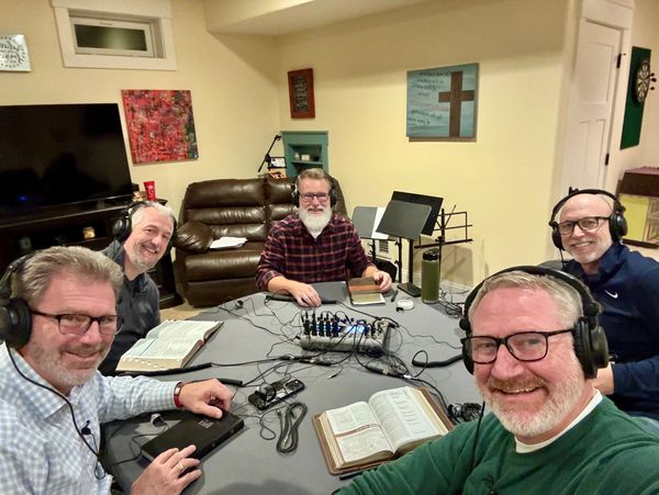 Five men with headphones around a table with Bibles and audio equipment.