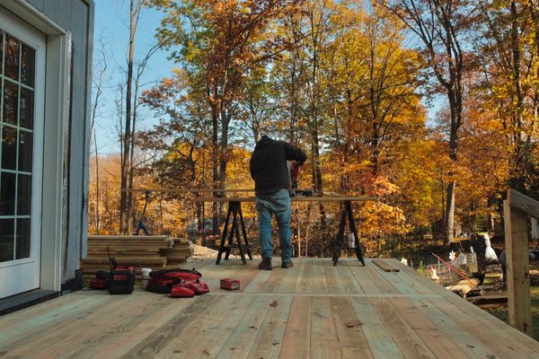 A man works on a wooden deck surrounded by autumn trees.