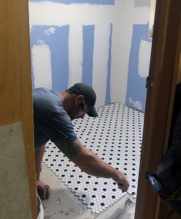 Man installing black and white hexagonal floor tiles in a room under renovation.