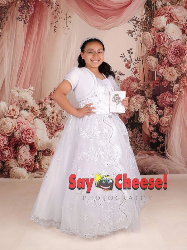 A girl in a white dress posing with a floral backdrop.