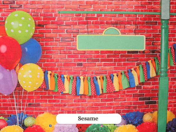 Colorful balloons and fabric garlands against a red brick wall backdrop.