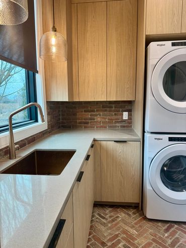 Laundry featuring light wooden cabinets, a built-in sink, and a dark-red brick-like wall and floor.