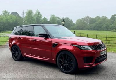 Red Range Rover SUV parked on a driveway with greenery in the background.