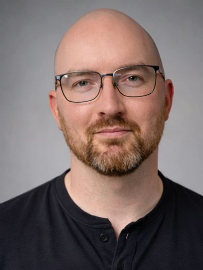 Portrait of a bald man with glasses and a beard wearing a black shirt.