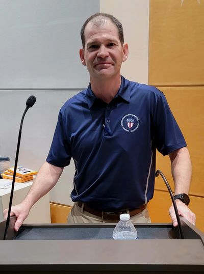 Man standing at a podium with microphones and a water bottle.