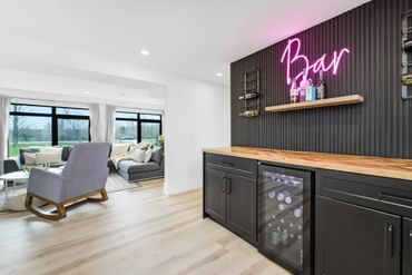 Modern home bar with neon sign and cozy living room.