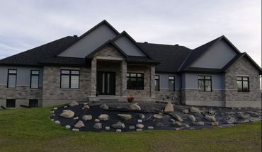 Modern stone and stucco house with a large front yard under landscaping.