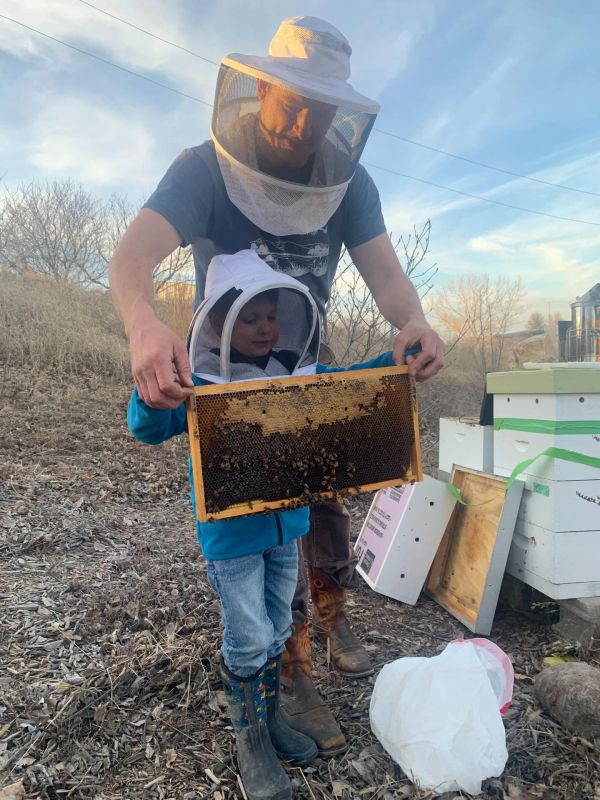 Adult and child in beekeeping gear holding a honeycomb frame.