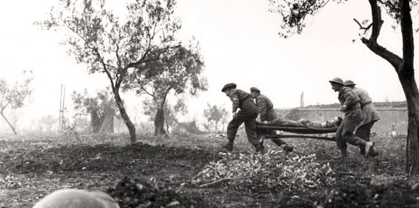 Soldiers carrying a wounded comrade on a stretcher through a battlefield with trees.