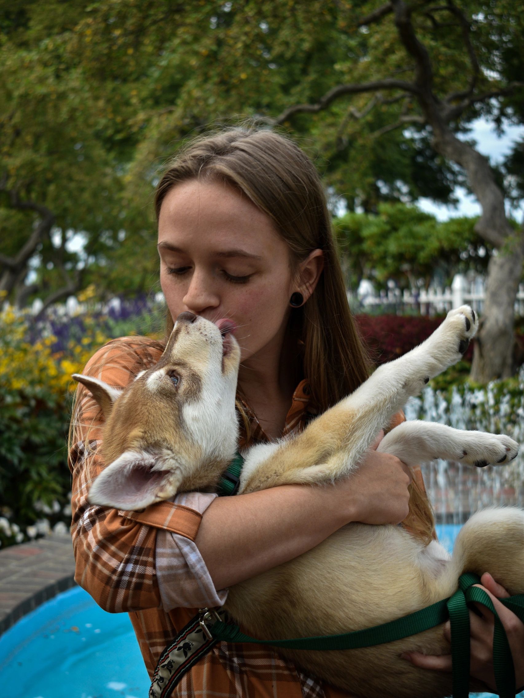 A woman lovingly holds and shares a kiss with her dog outdoors.