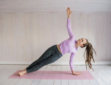 Woman doing a side plank yoga pose on a pink mat indoors.