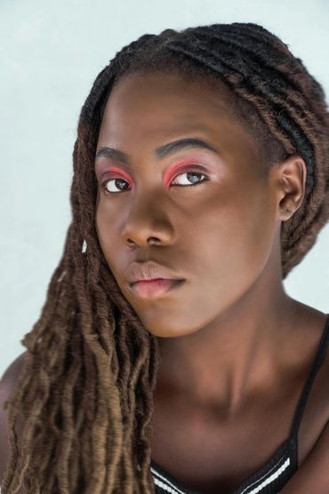 Close-up portrait of a woman with long dreadlocks and striking red eyeshadow.