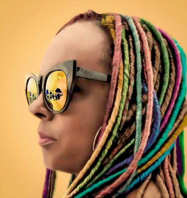 Profile of a woman with colorful dreadlocks and reflective sunglasses.