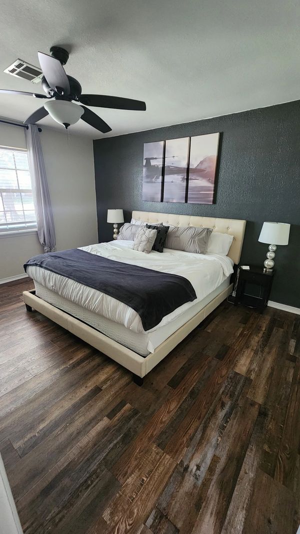 Modern bedroom with a large bed, dark accent wall, and wood flooring.