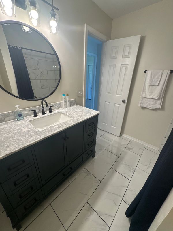 Modern bathroom with marble countertop and round mirror.