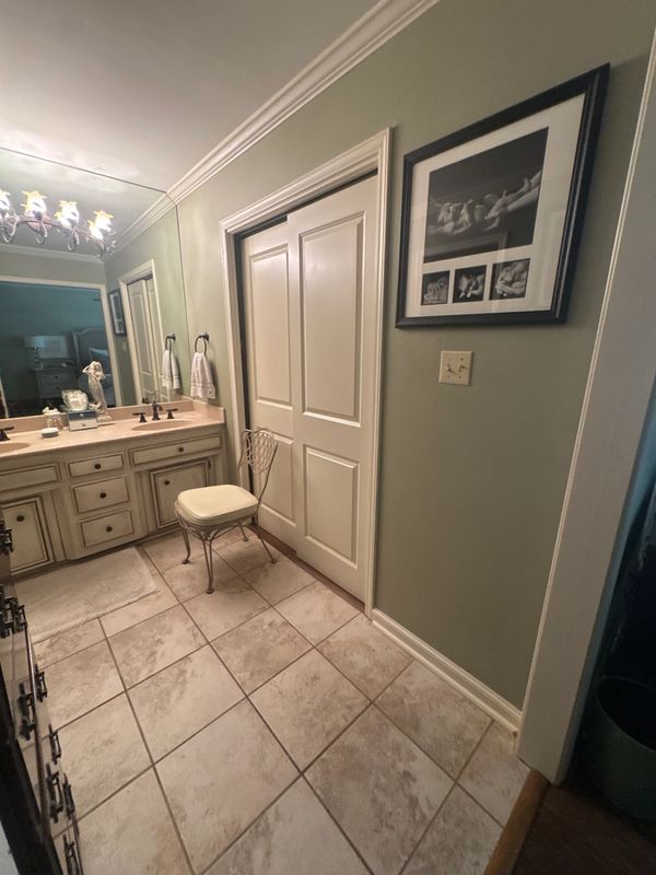Elegant bathroom with beige tiles, a cushioned chair, and a large mirror above the sink.