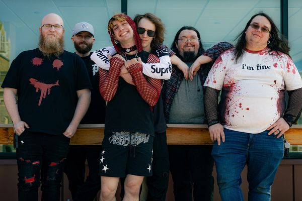 Group of six casually dressed friends posing together outdoors.