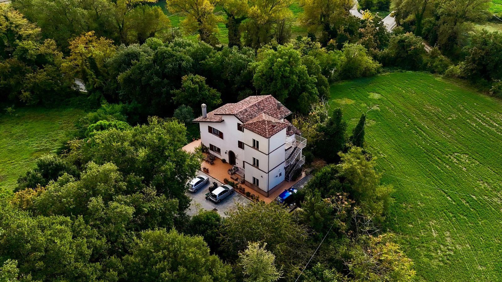 A white house surrounded by dense green trees and fields.