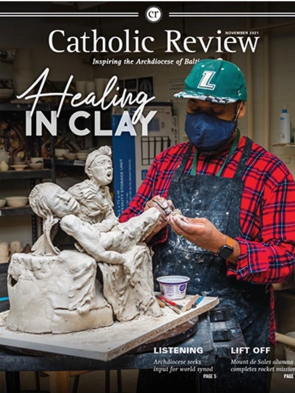Artist sculpts a detailed clay figure on Catholic Review cover.