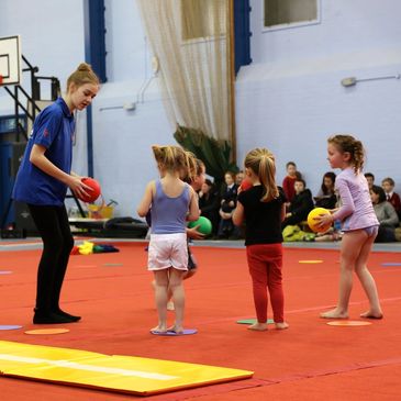 A gymnastics instructor with three children holding colorful inflated balls