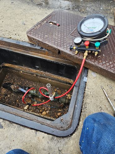 Water meter testing setup with pressure gauge and valves in an open manhole.